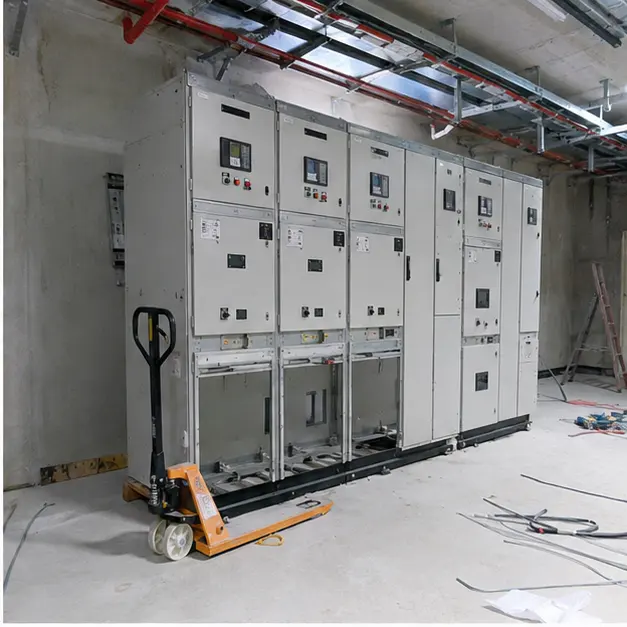 Technicians positioning and aligning metal-clad switchgear panels on a base channel inside an electrical room