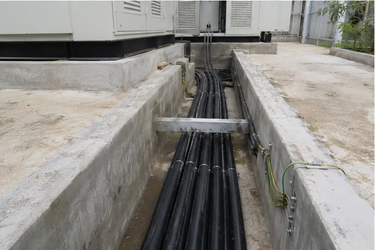 Open cable trench beside a compact substation with medium- and low-voltage cables and earthing conductors